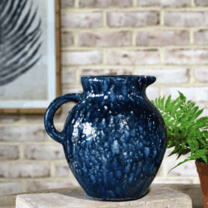 A dark blue ceramic pitcher with a speckled pattern on a table.